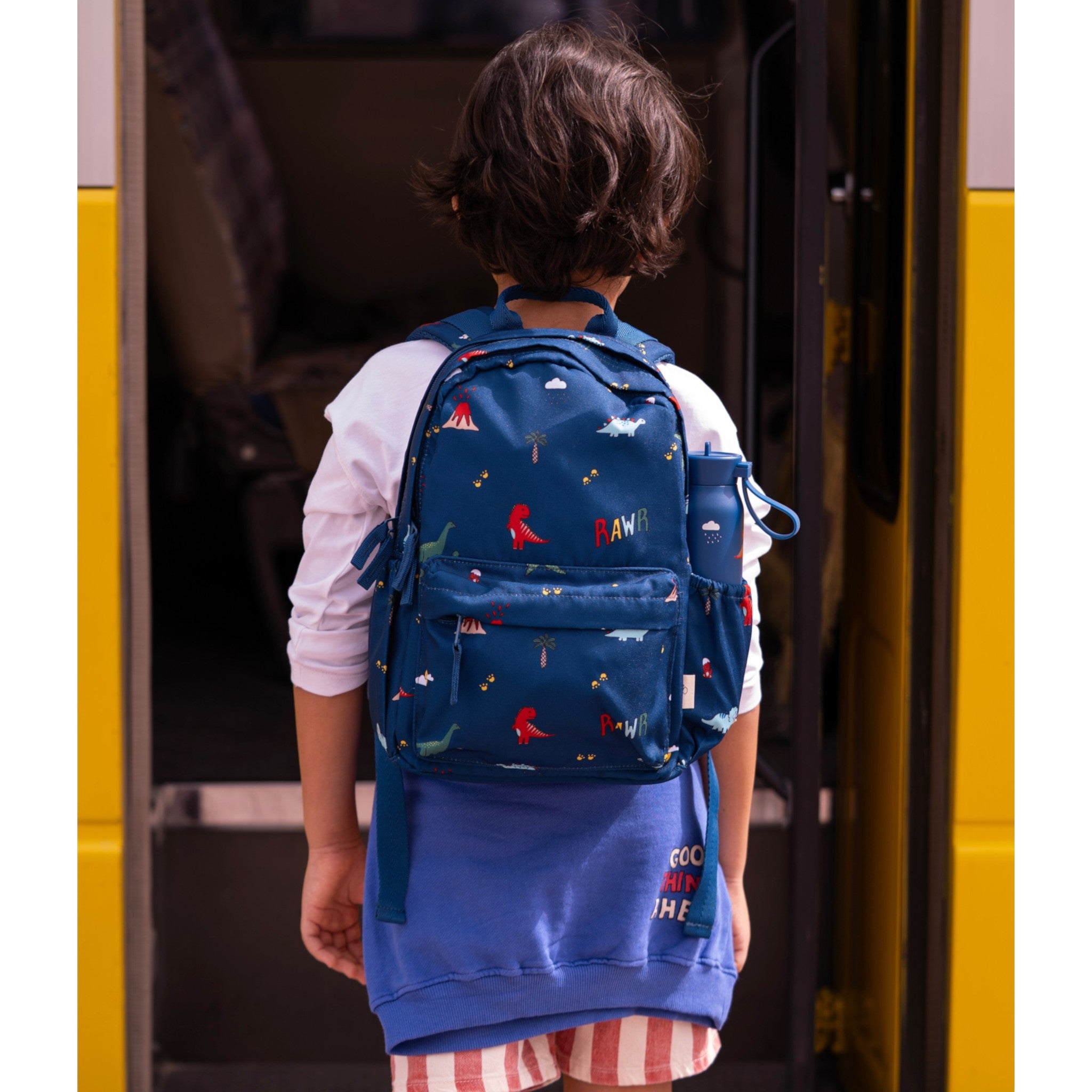 Child wearing a Lil Bunnies - The Collective blue medium backpack featuring a colourful dinosaur print