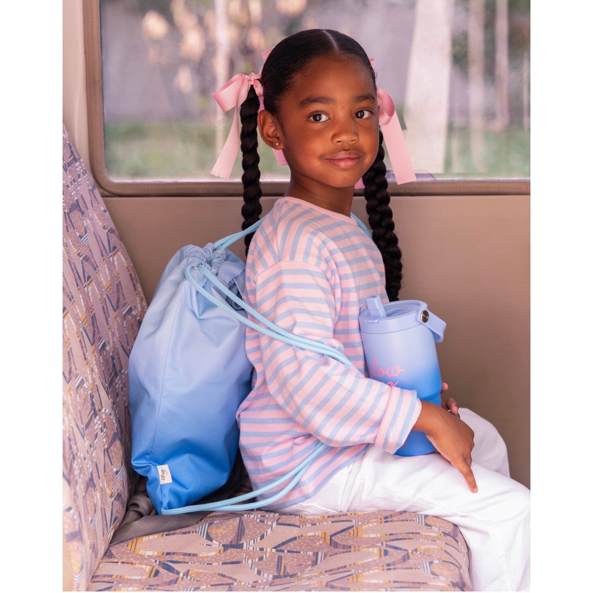 Young girl holding a Lil Bunnies - The Collective blue insulated tumbler with a matching ombre drawstring bag