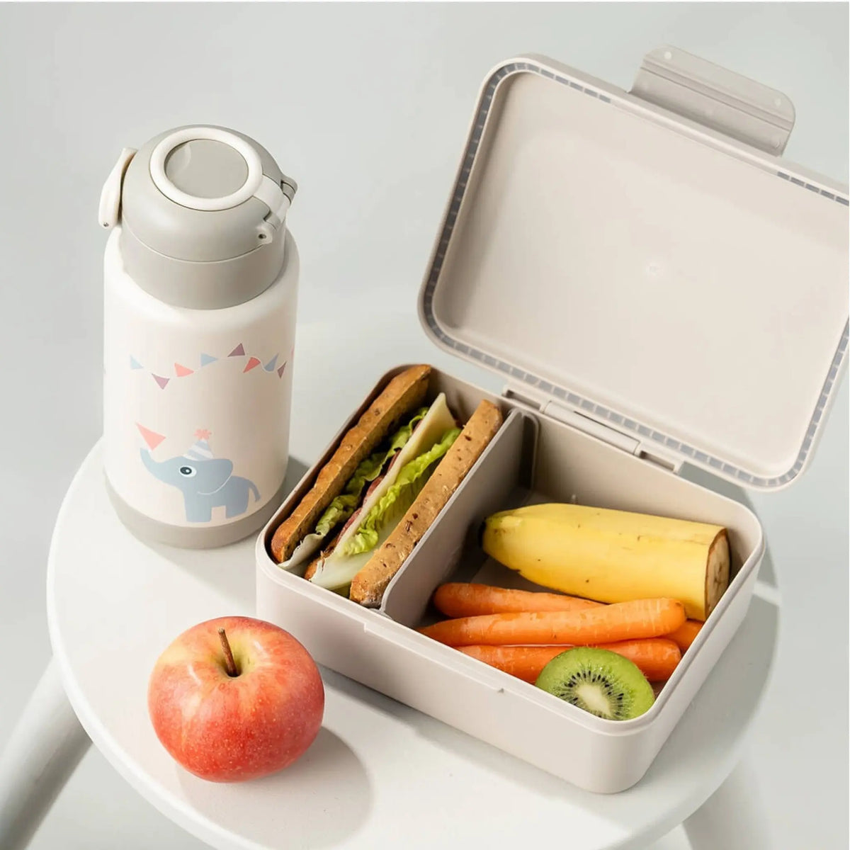 Lil Bunnies - The Collective sand-colored insulated bottle with elephant print next to a matching lunch box with food.