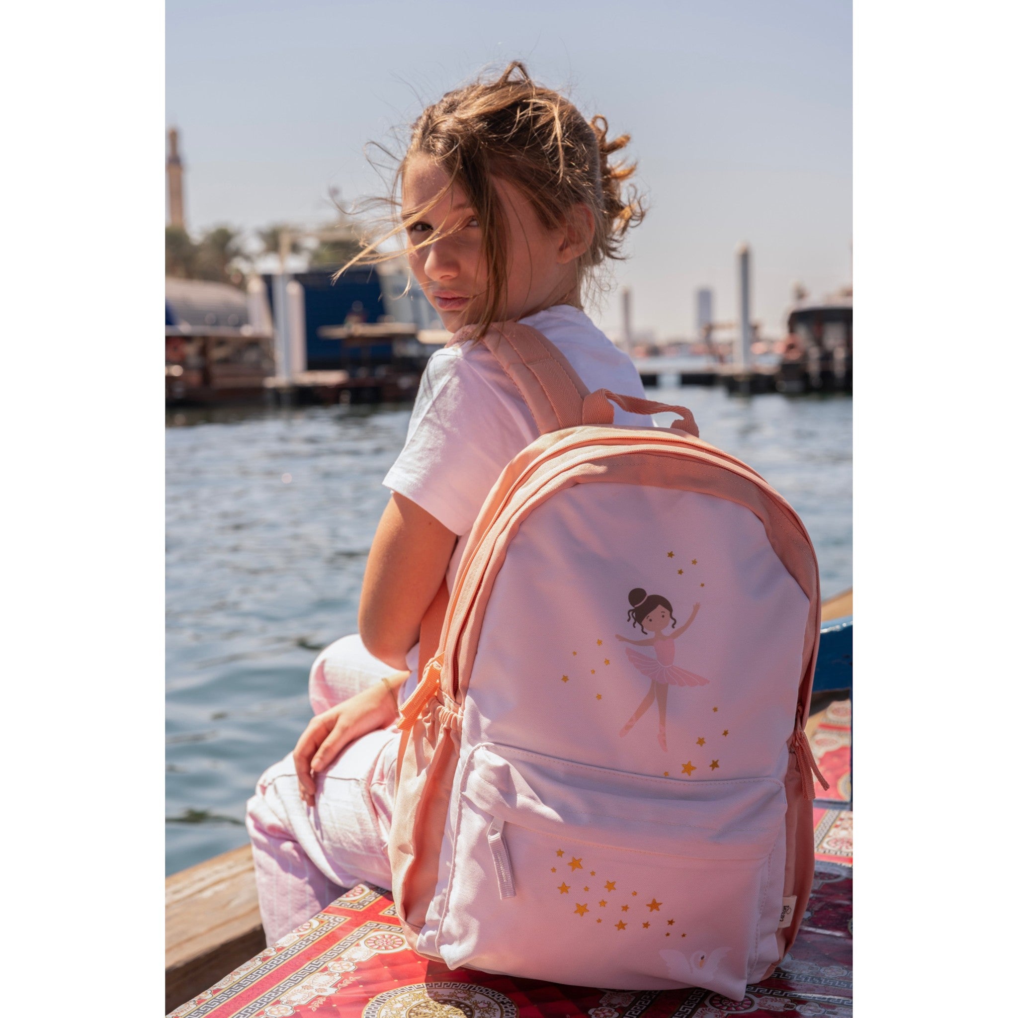 Young girl wearing a light pink Lil Bunnies - The Collective Grand Backpack featuring a ballerina and gold stars.