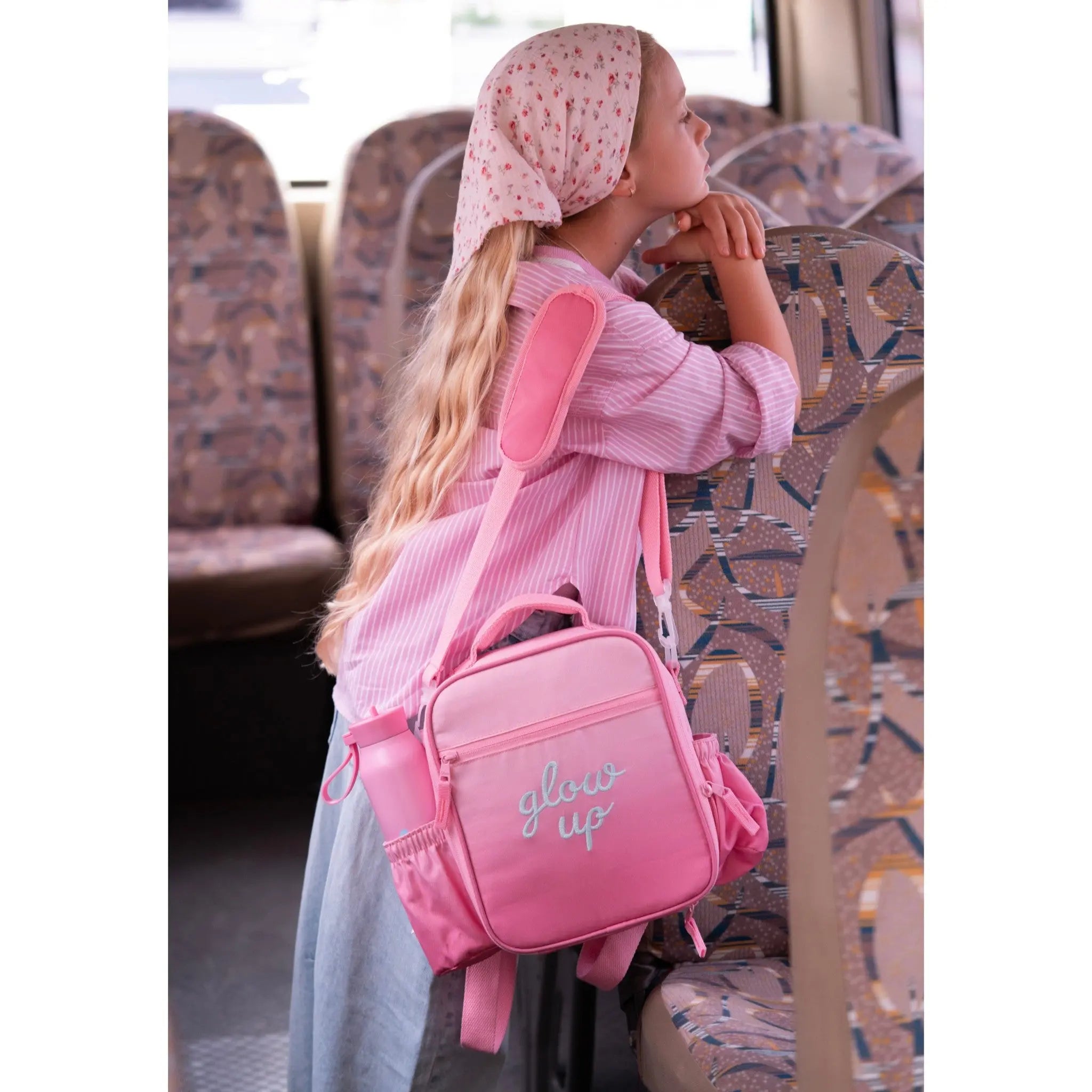 Young girl wearing a Lil Bunnies - The Collective pink insulated lunchbag backpack with Glow Up embroidery on a bus.