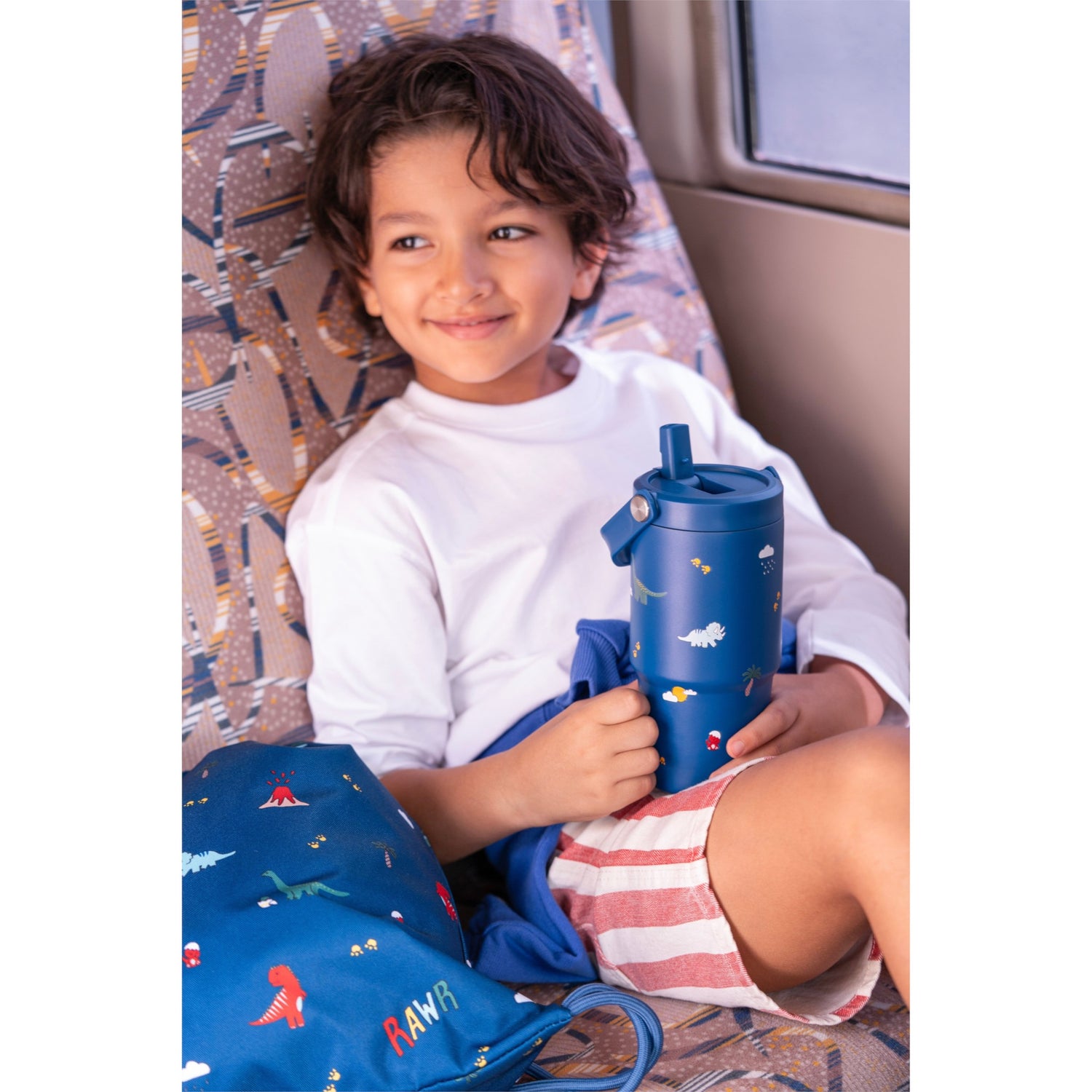 Child holding a blue Lil Bunnies - The Collective 600ml insulated tumbler with dinosaur patterns and a straw lid