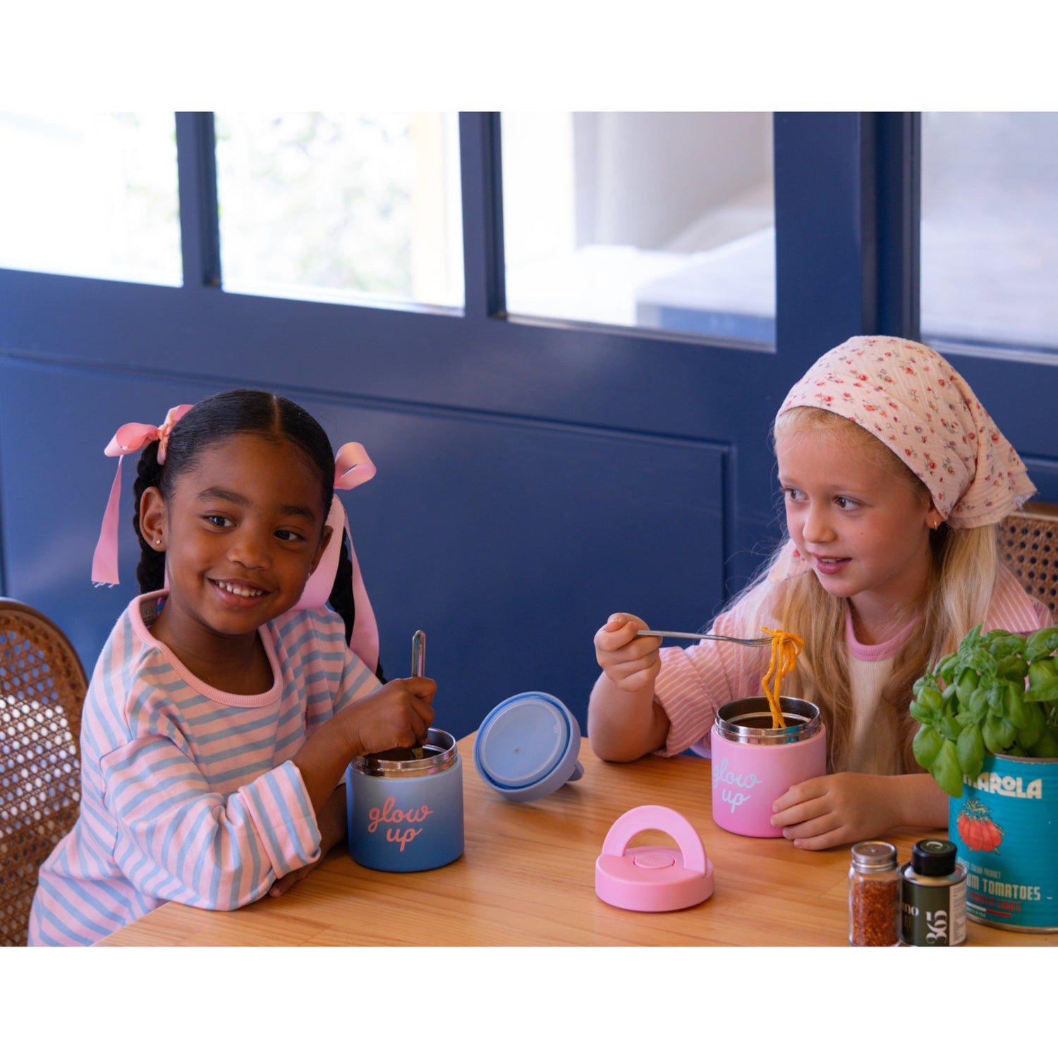 Two girls eating from Lil Bunnies - The Collective blue and pink insulated stainless steel food jars at a table