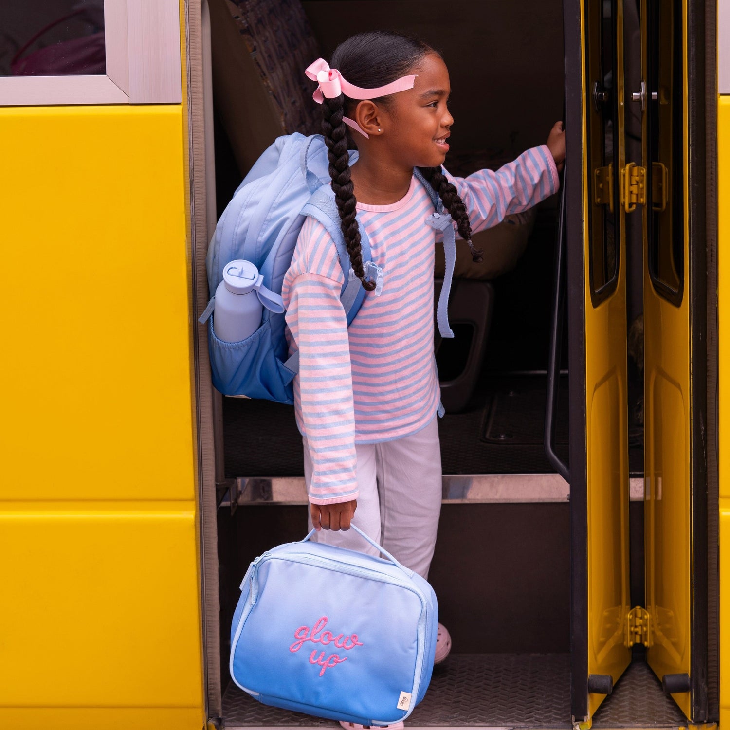 Lil Bunnies - The Collective blue insulated square lunch bag with glow up text held by a girl boarding a school bus