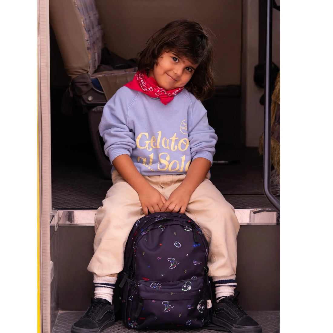 Child sitting on a Lil Bunnies - The Collective medium gaming backpack with colorful controller icons on black fabric