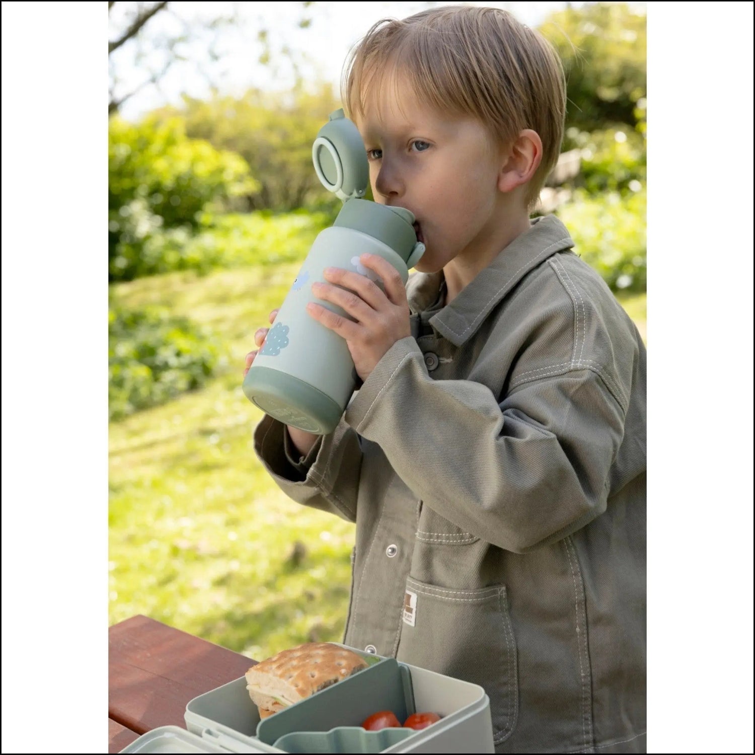 Young boy drinking from a Lil Bunnies - The Collective sage green insulated water bottle with cloud print outdoors.