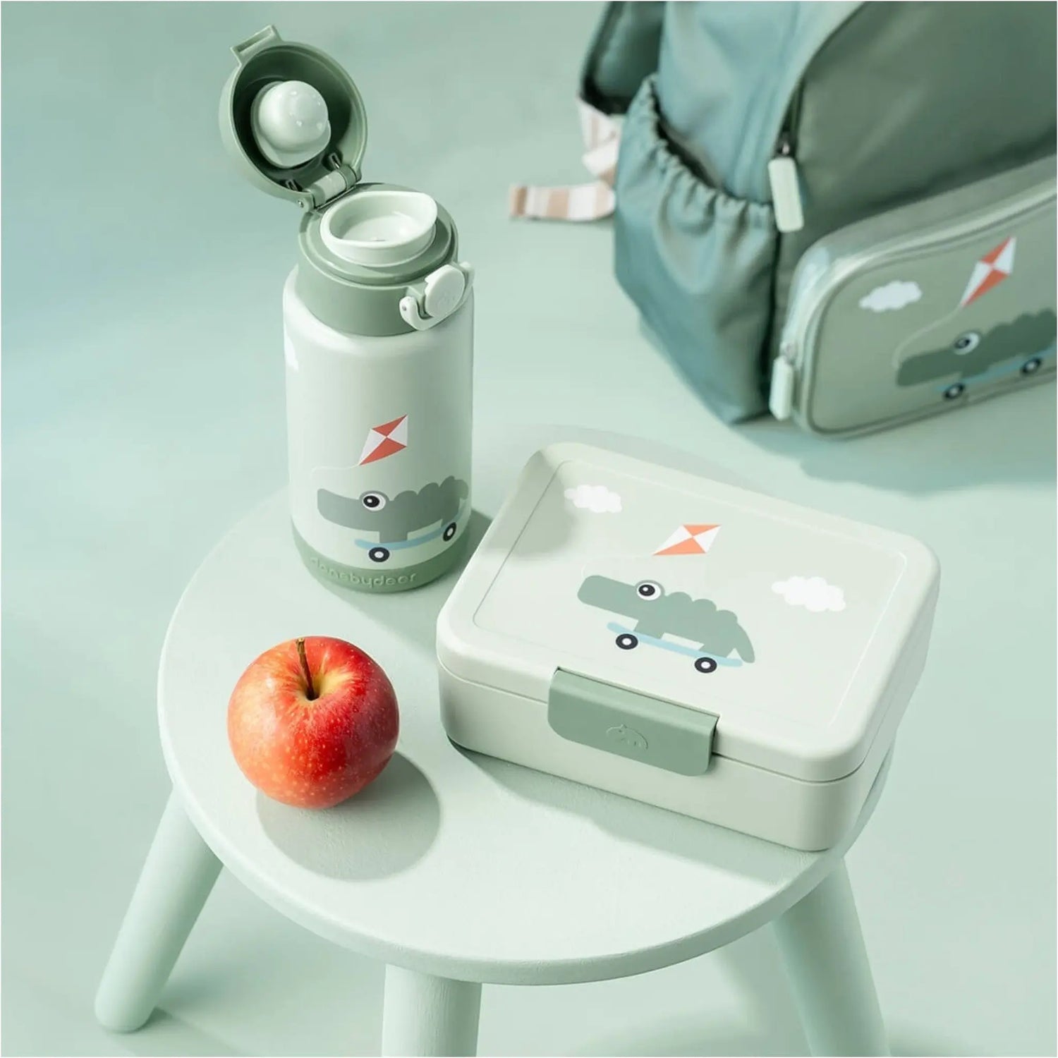 Lil Bunnies - The Collective green insulated bottle with crocodile print next to a matching lunch box and an apple