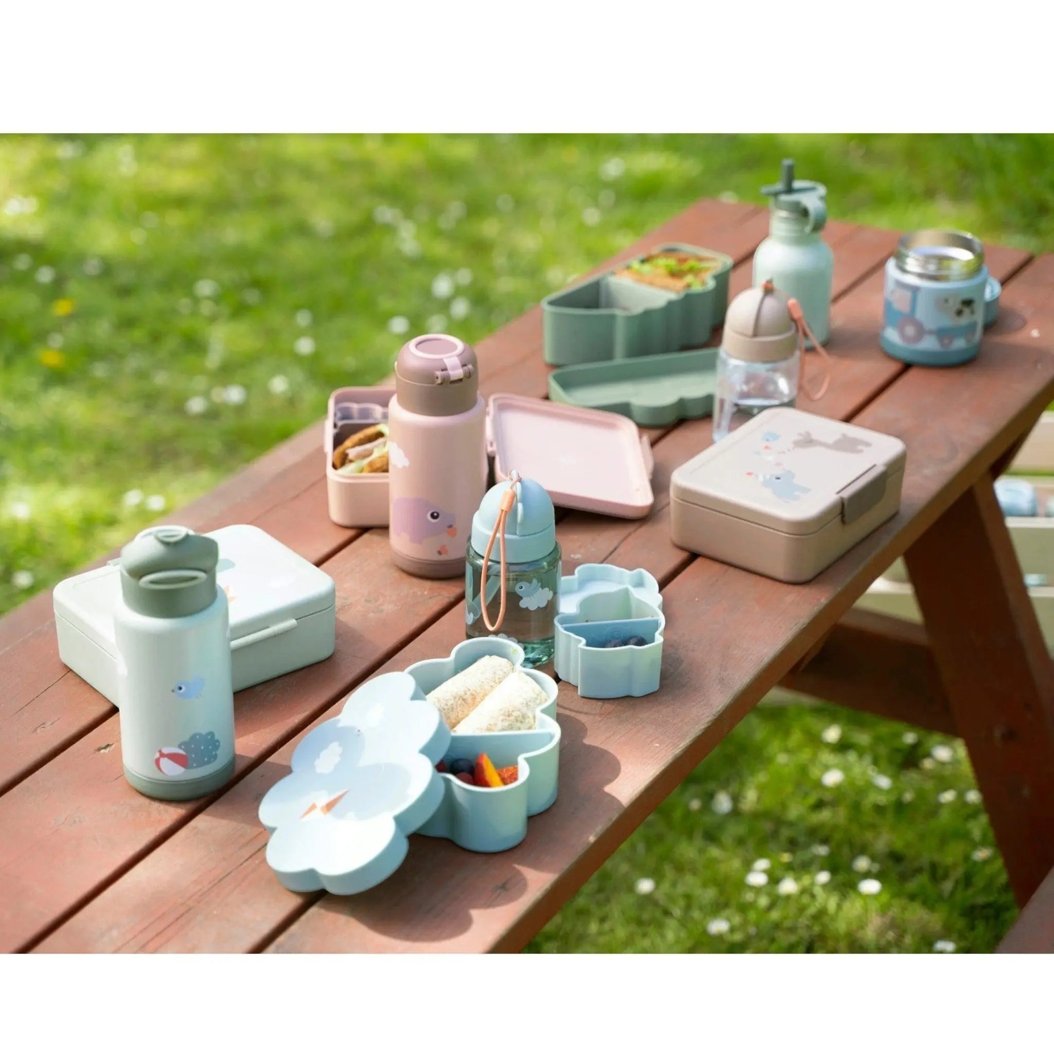 Lil Bunnies - The Collective green insulated bottle displayed on a wooden picnic table with matching lunch containers.