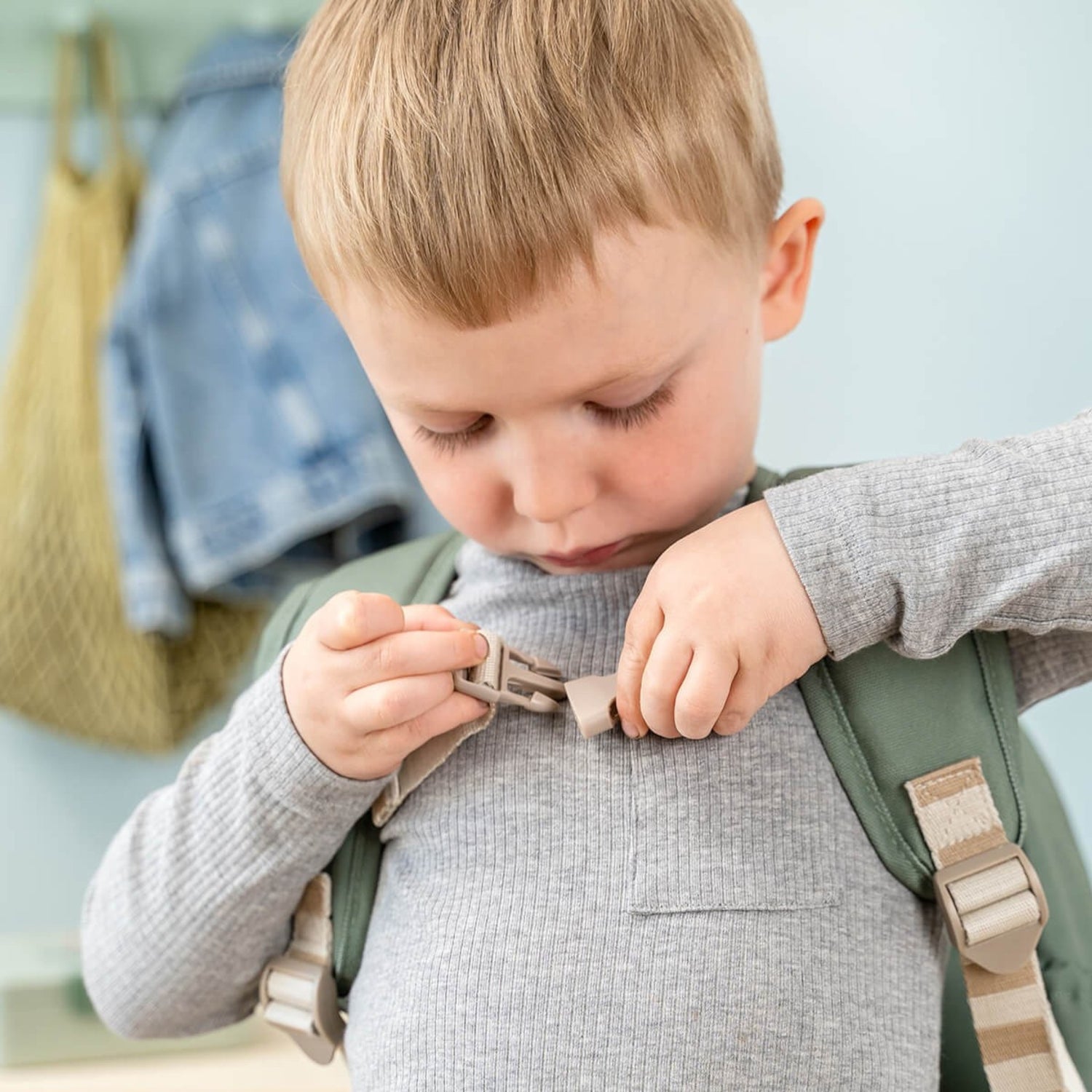 Young boy wearing a Lil Bunnies - The Collective green kids backpack, fastening the chest strap buckle