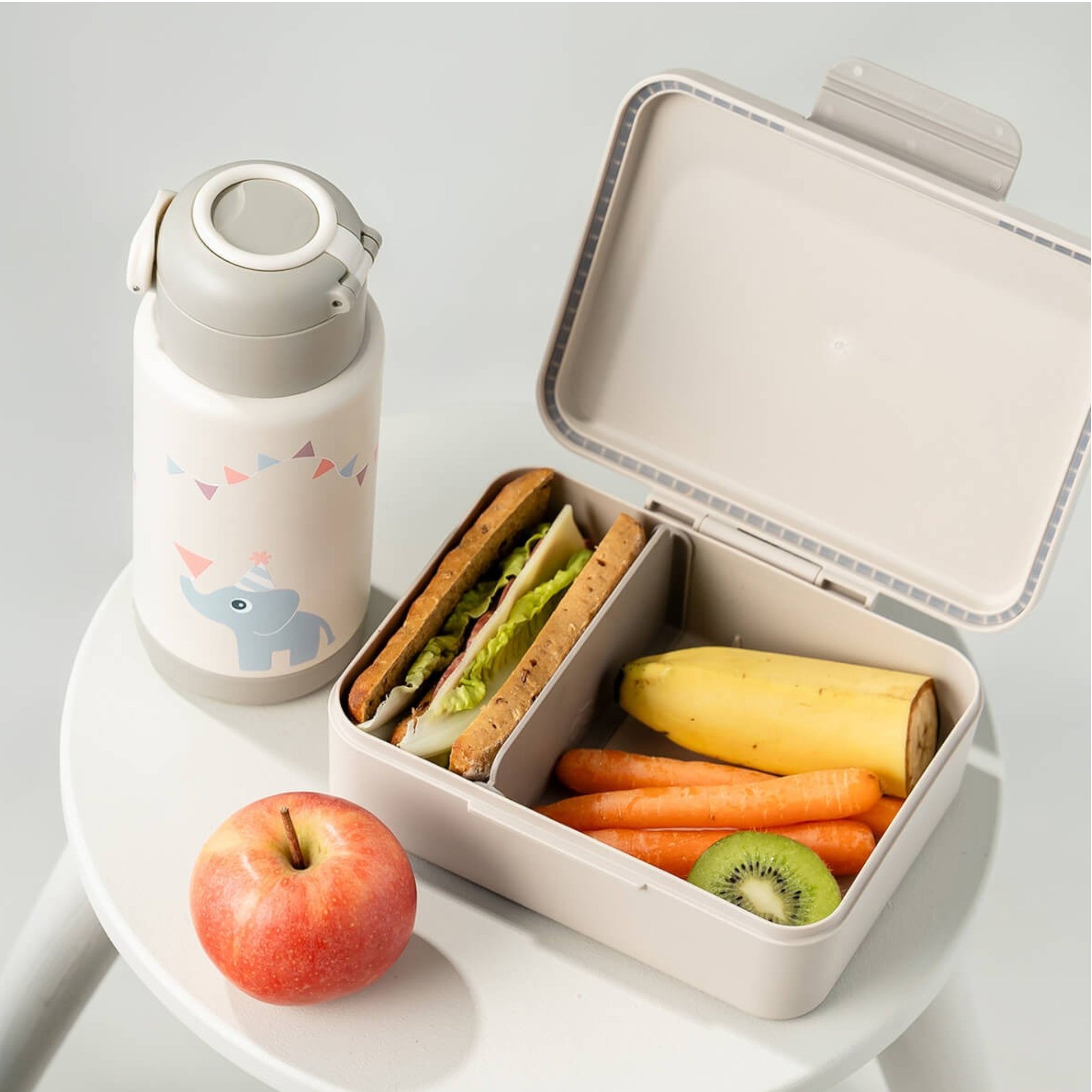 Lil Bunnies - The Collective sand-colored insulated bottle with elephant print next to a matching lunch box with food.