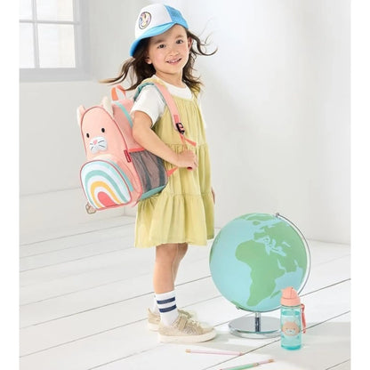 Young girl wearing a pink Lil Bunnies - The Collective cat-themed zoo backpack with a rainbow design