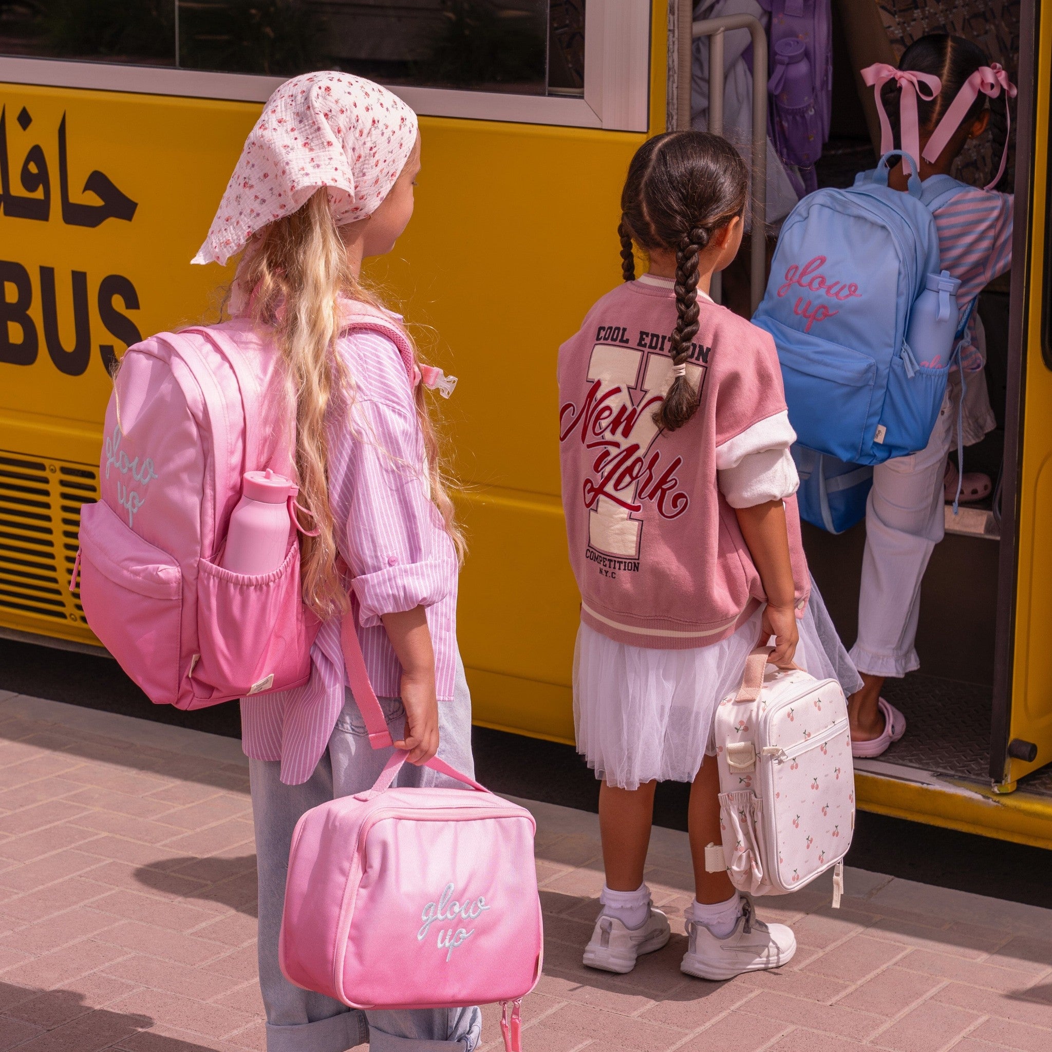 Lil Bunnies - The Collective pink insulated square lunch bag held by a young girl boarding a yellow school bus