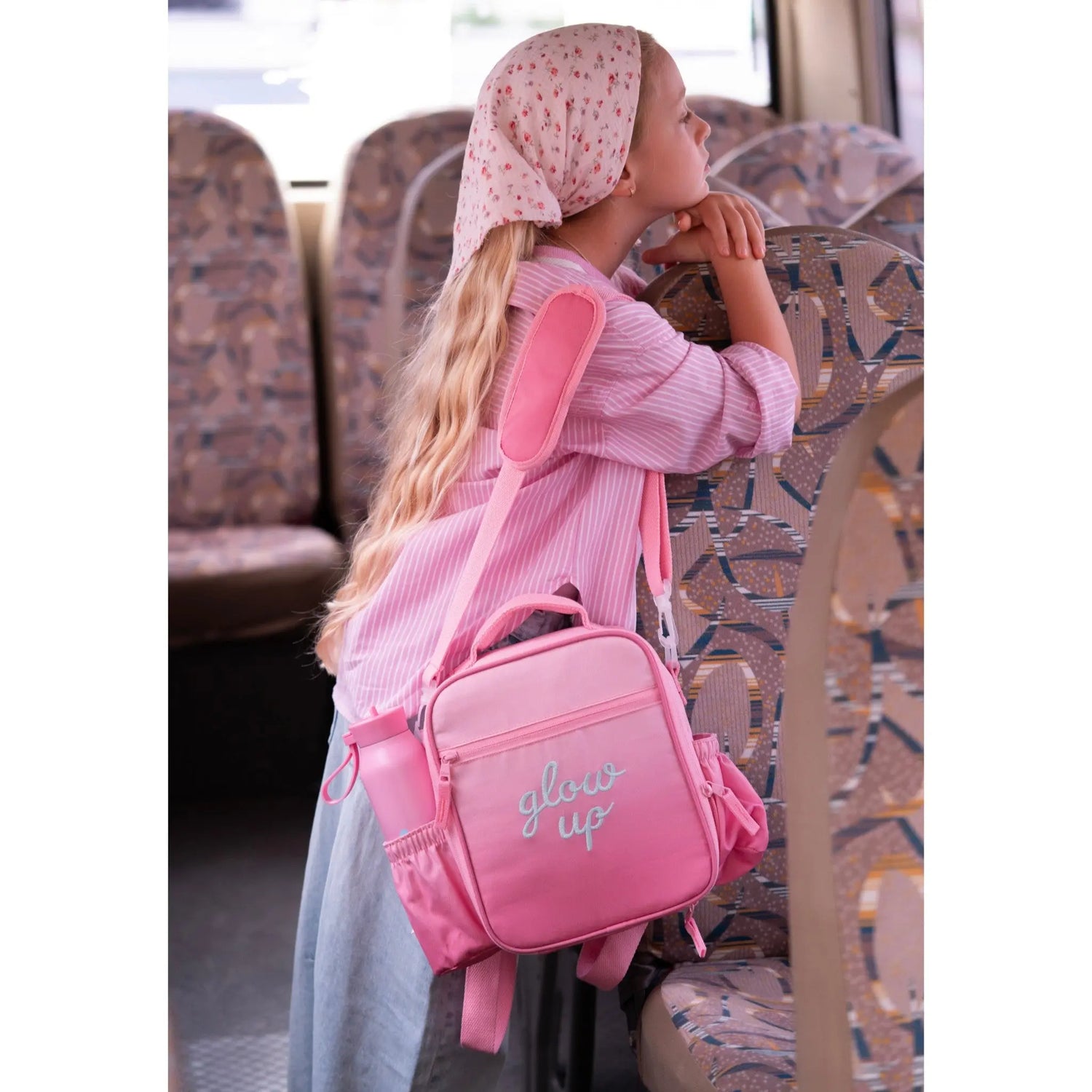 Young girl wearing a Lil Bunnies - The Collective pink insulated lunchbag backpack with Glow Up embroidery on a bus.