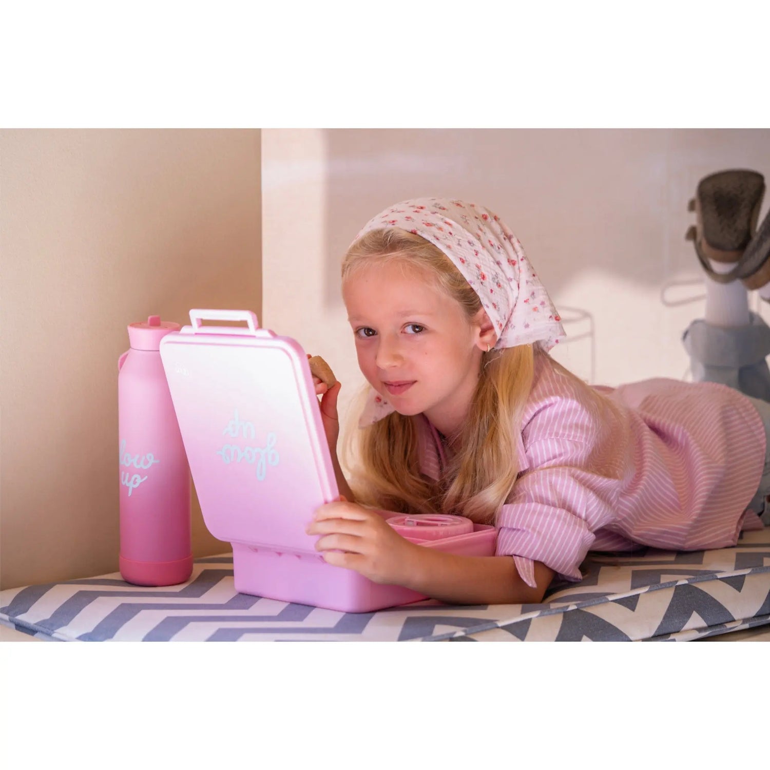 Young girl with a headscarf holding a Lil Bunnies - The Collective pink insulated lunchbox and matching food jar