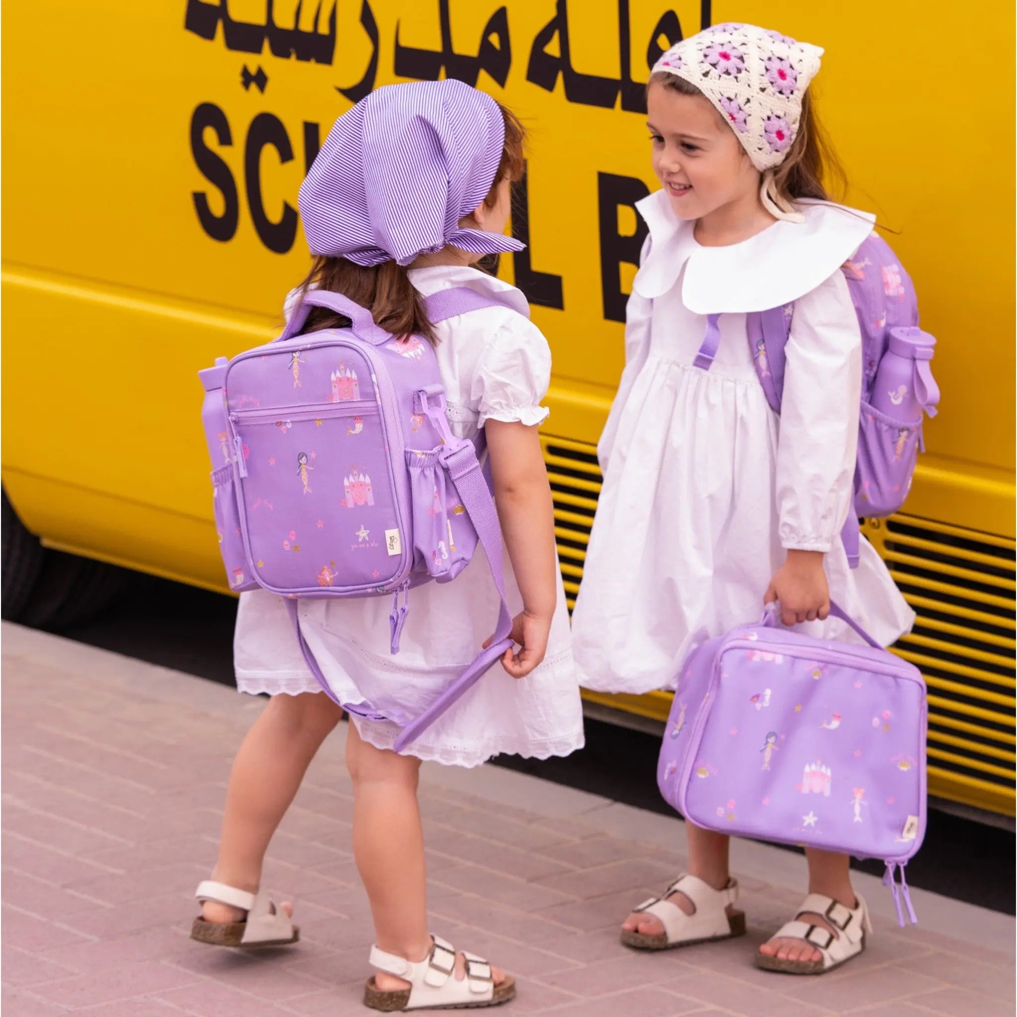 Two girls wearing white dresses and Lil Bunnies - The Collective purple mermaid insulated square lunch bags