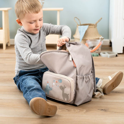 Young boy sitting on a wooden floor opening a sand-colored Lil Bunnies - The Collective kids backpack with animal art