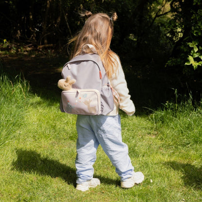 A young girl wearing a Lil Bunnies - The Collective sand-coloured kids backpack with animal illustrations outdoors.