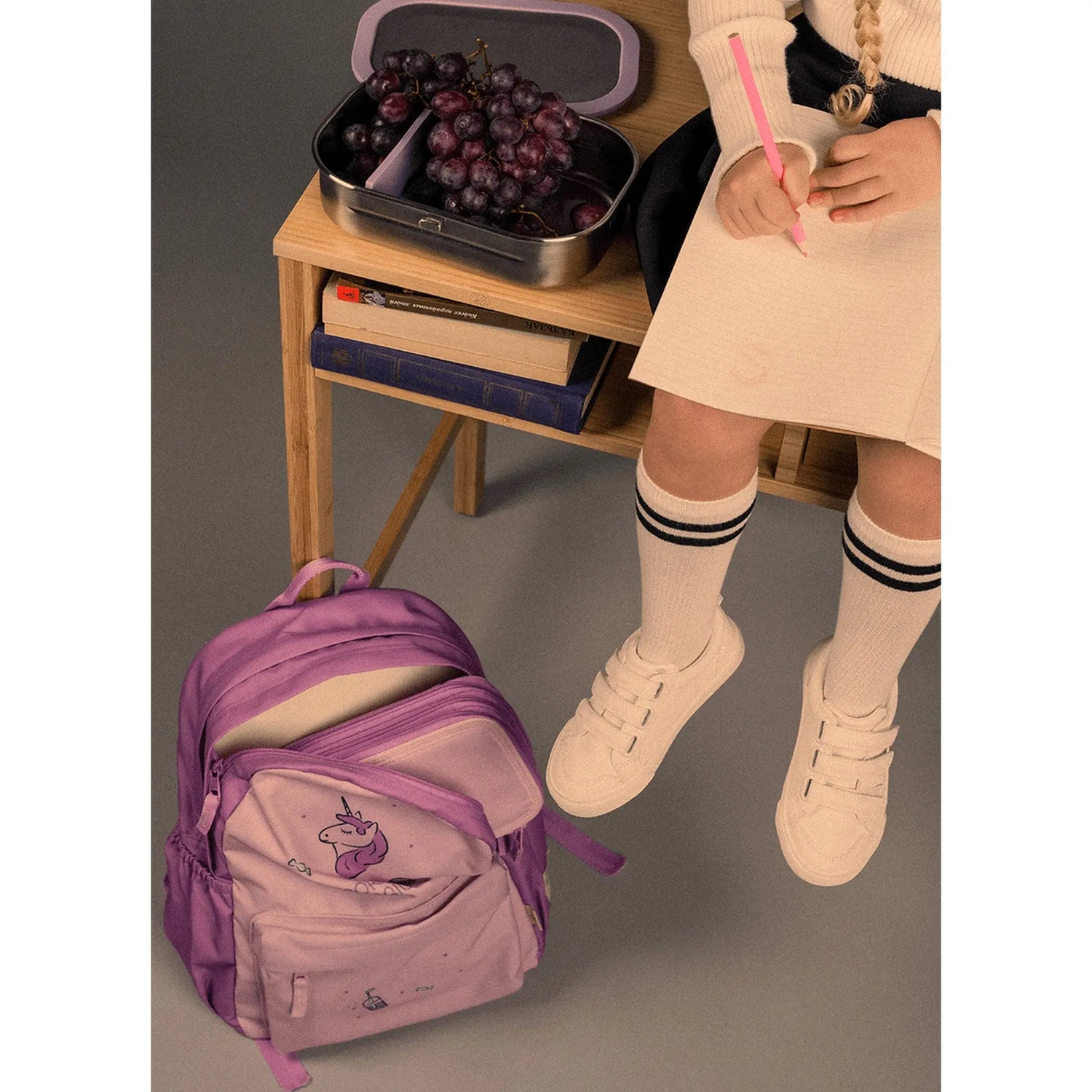 Lil Bunnies - The Collective Grand Backpack in stormy purple with a unicorn print, shown next to a child at a desk.