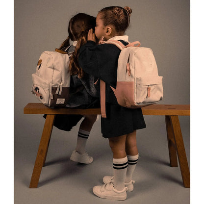 Two children wearing Lil Bunnies - The Collective beige vehicle-themed mini backpacks while sitting on a wooden bench.