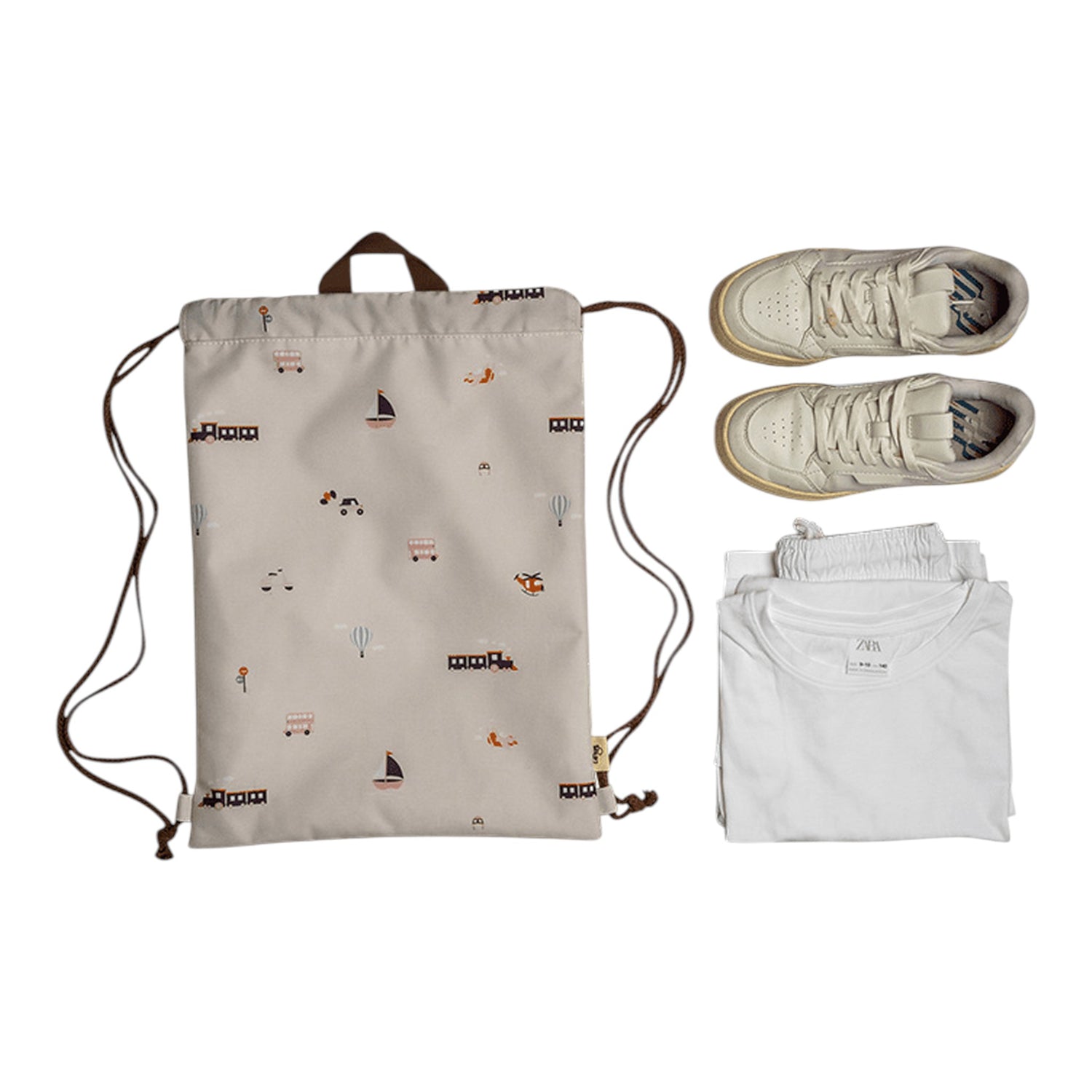 Lil Bunnies - The Collective drawstring wet bag in beige with a vehicles print, next to white clothes and sneakers.